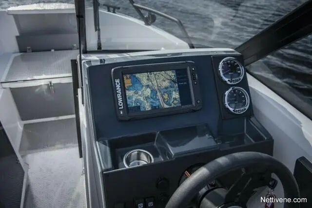 Boat dashboard featuring a Lowrance navigation screen with a map, two gauges, and a steering wheel, by the water.